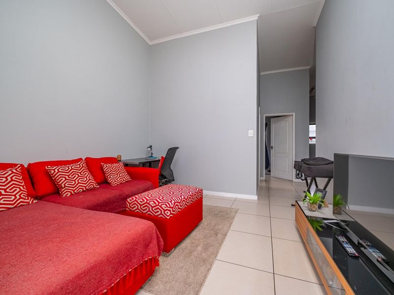 A living room featuring neutral wall paint, tiled flooring, and coved ceilings, providing a functional space with access to an adjoining hallway.