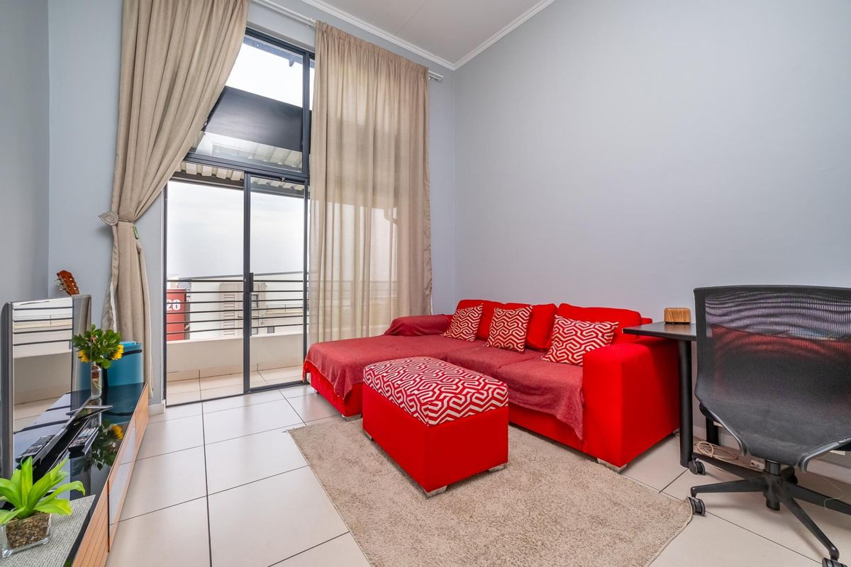 A bright living room featuring large sliding glass doors that provide access to a balcony, complemented by neutral tiled flooring and high ceilings.