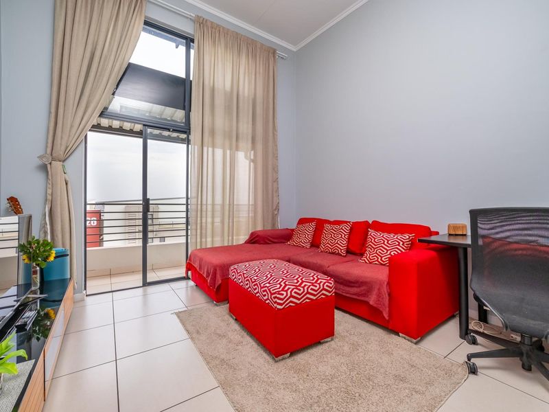 A bright living room featuring large sliding glass doors that provide access to a balcony, complemented by neutral tiled flooring and high ceilings.