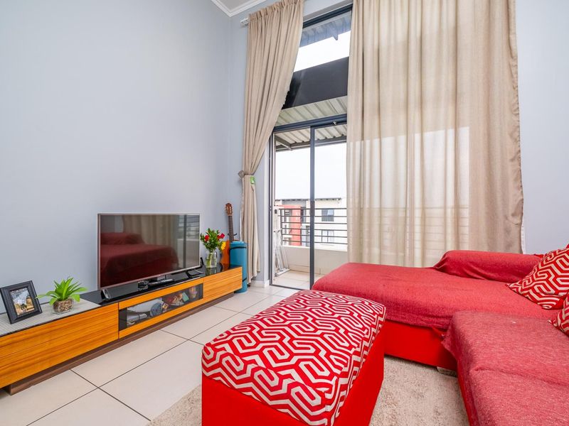 A bright living room featuring high ceilings, large sliding glass doors leading to a balcony, and neutral tiled flooring.