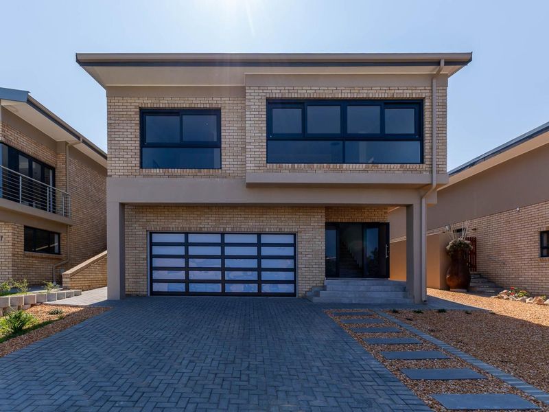 Modern double-story brick house featuring a paved driveway, a contemporary sectional garage door, and large sliding windows.