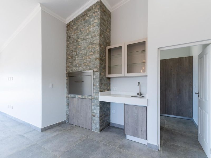 A modern indoor entertainment area featuring a built-in braai with stone cladding, a sleek wet bar with sink, and neutral tiled flooring.
