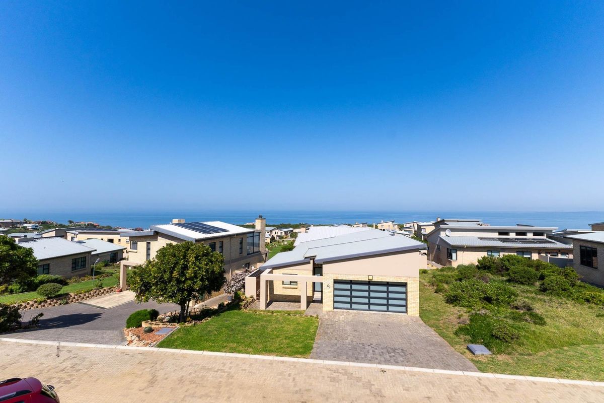 Aerial view of a modern residential property featuring a paved driveway, garage, and solar panels, set within a coastal estate with ocean views.