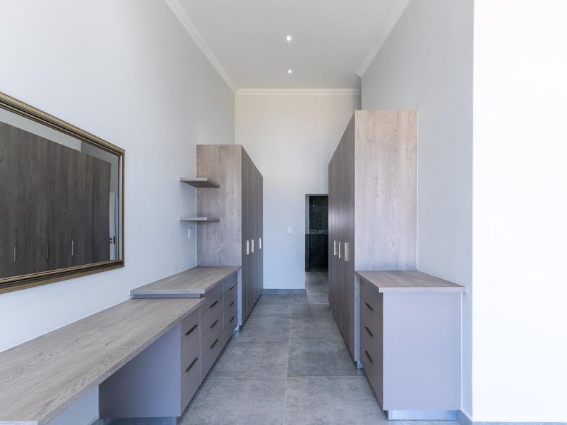 A modern, empty dressing room or walk-in closet featuring extensive built-in cabinetry, a vanity area, and neutral tiled flooring.