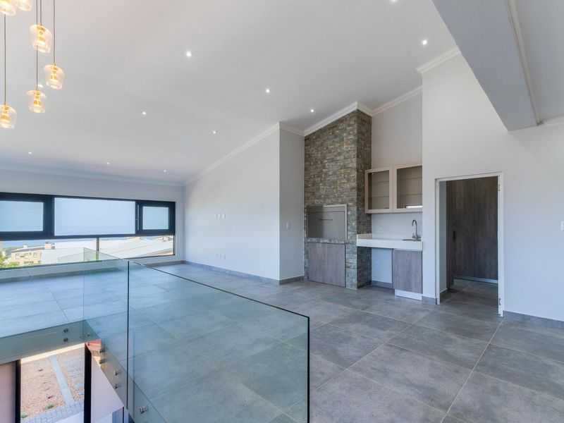 Spacious open-plan living area featuring a built-in braai with stone cladding, modern tiled floors, glass balustrade, and integrated cabinetry with a sink.