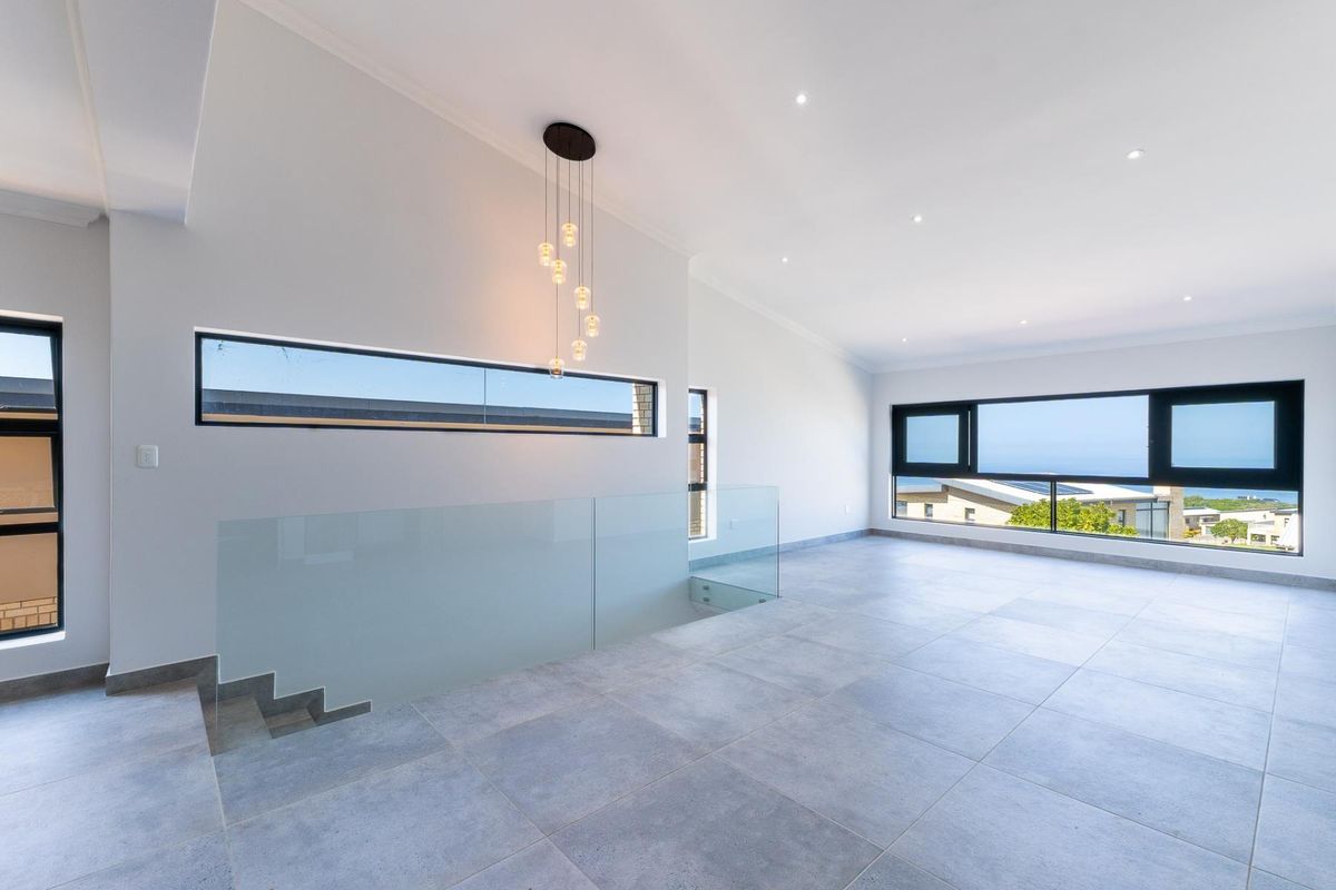 Spacious, modern open-plan living area featuring large windows, sleek tiled flooring, a glass balustrade, and contemporary lighting fixtures.