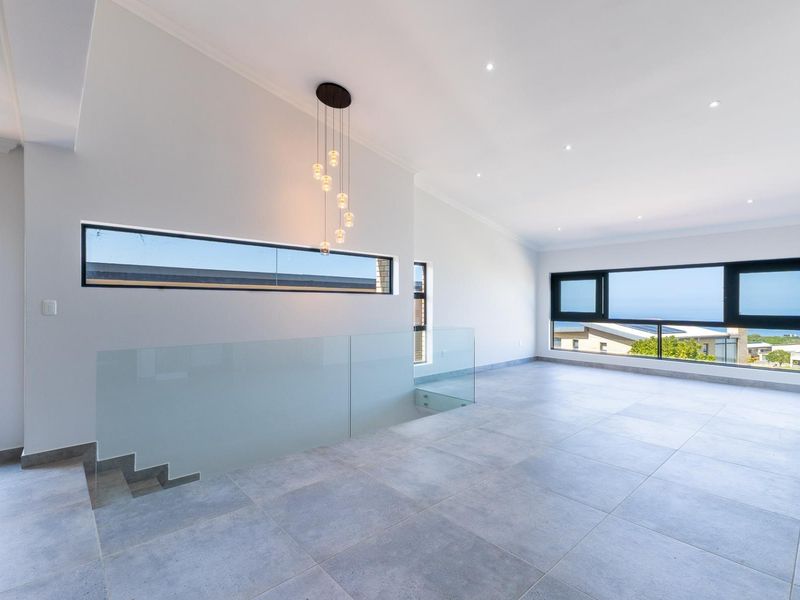 Spacious, modern open-plan living area featuring large windows, sleek tiled flooring, a glass balustrade, and contemporary lighting fixtures.