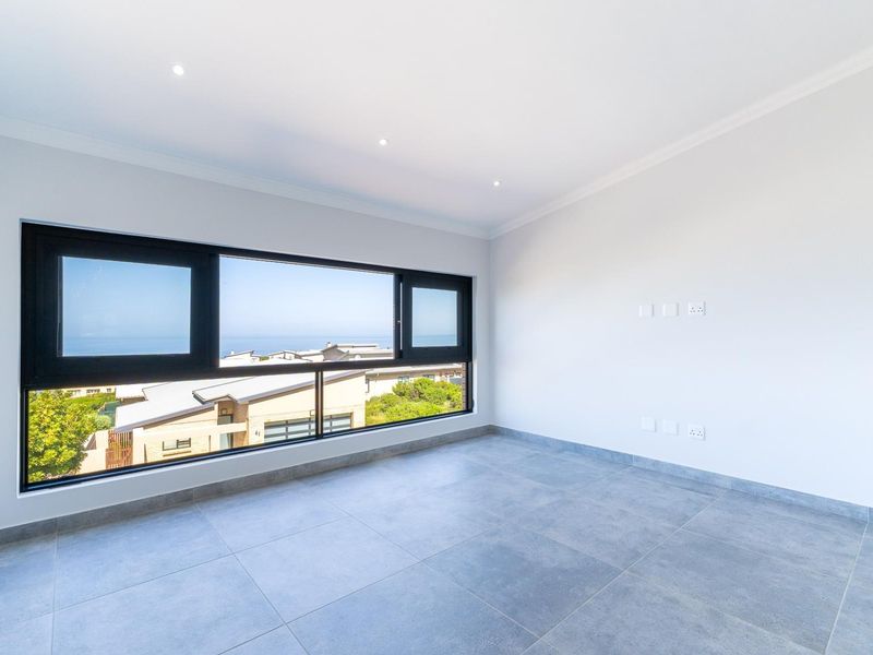 A bright, empty bedroom featuring large black-framed windows with scenic views, modern tiled flooring, and recessed downlighting.