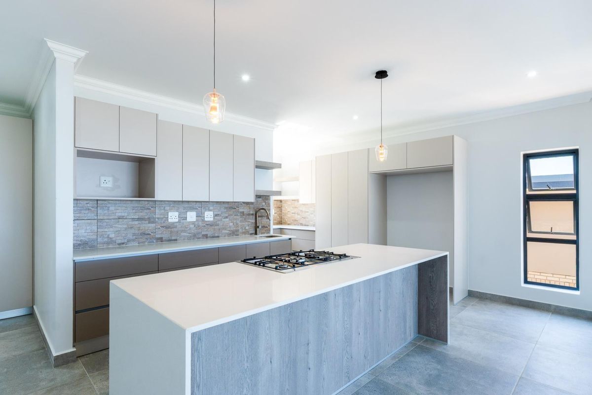 Modern kitchen featuring a central island with a gas cooktop, sleek built-in cabinetry, stone-look backsplash, and contemporary pendant lighting.