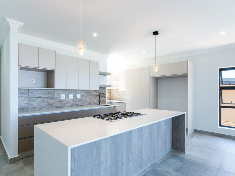 Modern kitchen featuring a central island with a gas cooktop, sleek built-in cabinetry, stone-look backsplash, and contemporary pendant lighting.