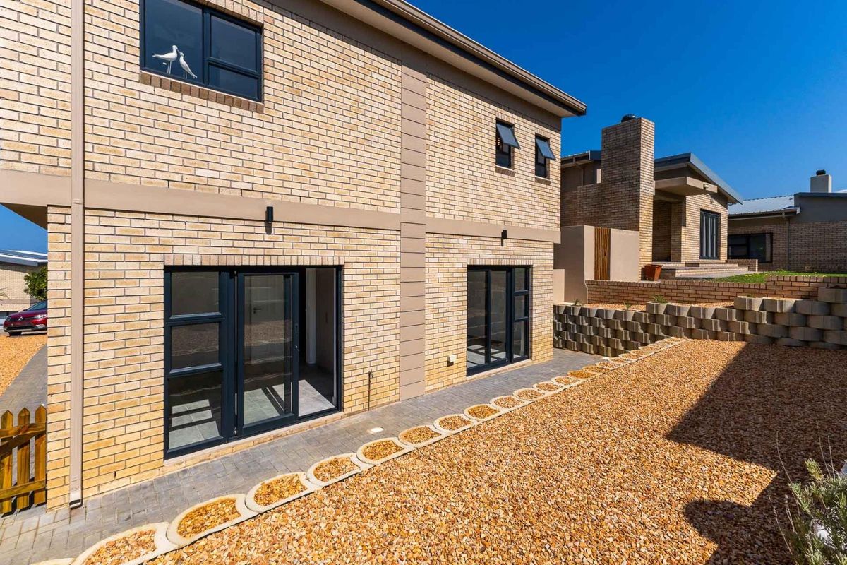 Rear view of a modern face brick house featuring aluminium framed doors and windows, a paved walkway, and a landscaped gravel garden area.