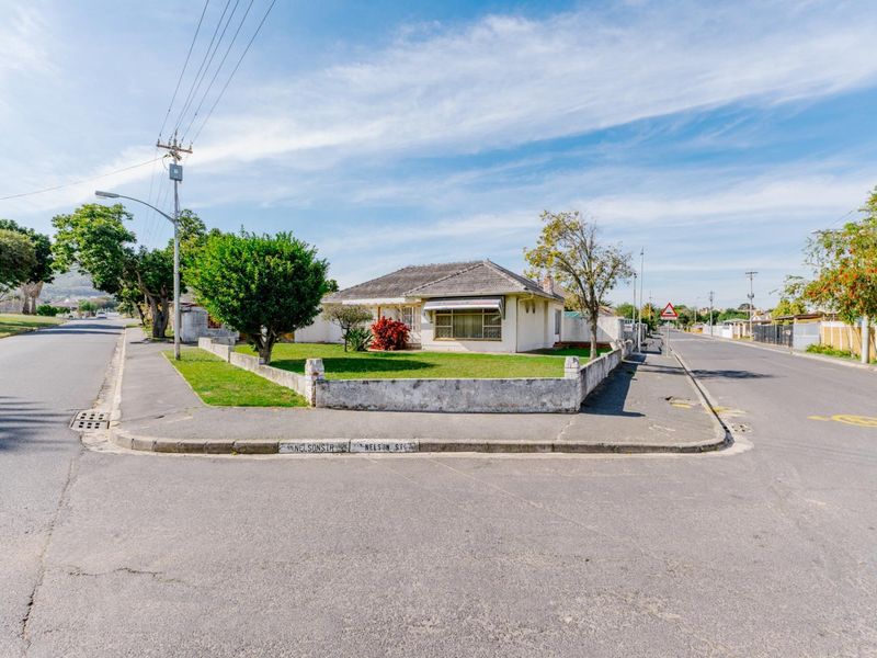 A corner-lot residential property featuring a single-story house with a tiled roof, front garden, and concrete boundary wall.