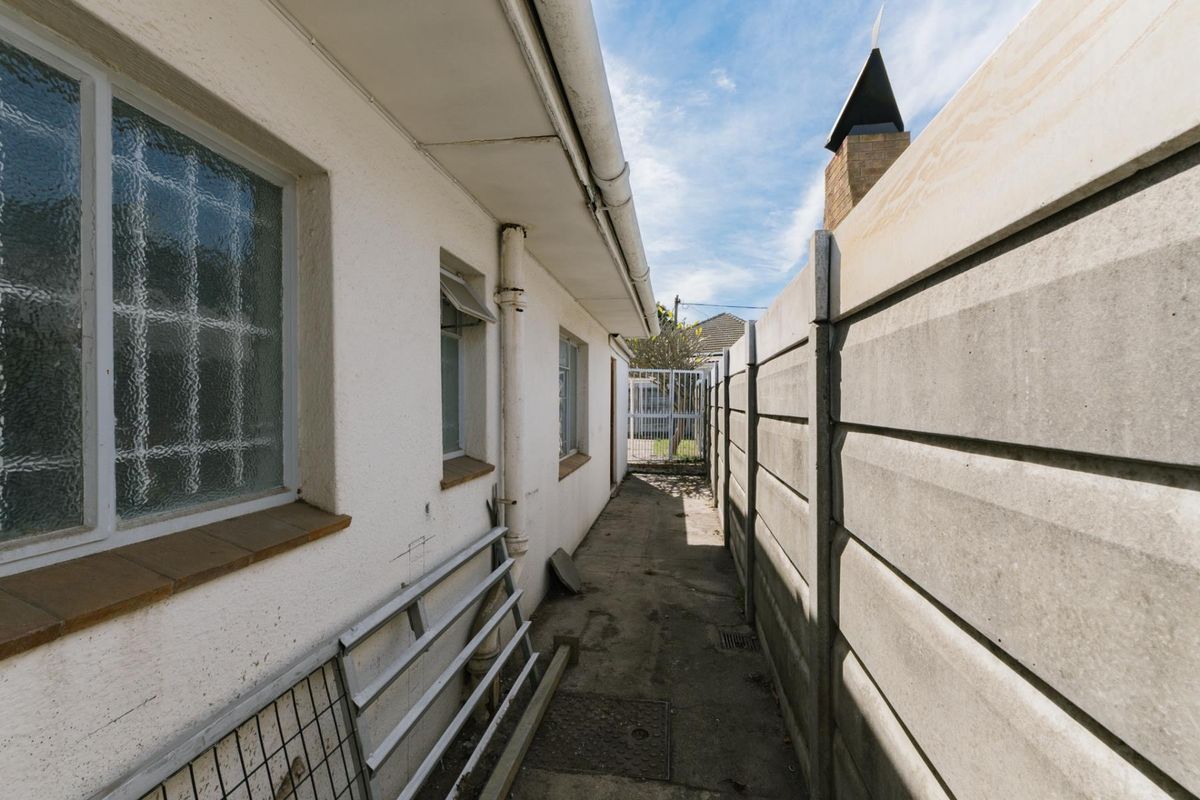 A narrow side passage featuring a precast concrete boundary wall, concrete paving, and exterior wall access with security-fitted windows.