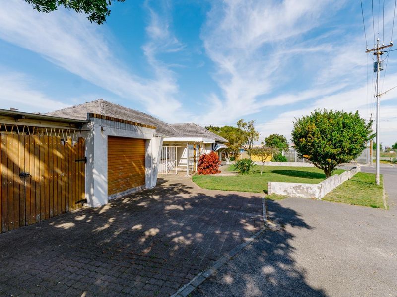 Front exterior view of the property featuring a paved driveway, attached garage, and a low boundary wall with a garden area.