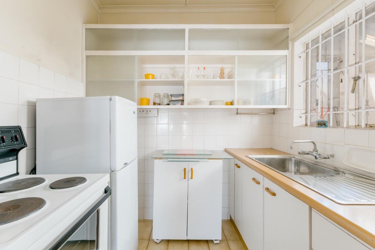 A compact, functional kitchen featuring white cabinetry, a stainless steel sink, tiled backsplash, and built-in shelving, offering potential for modern renovation.