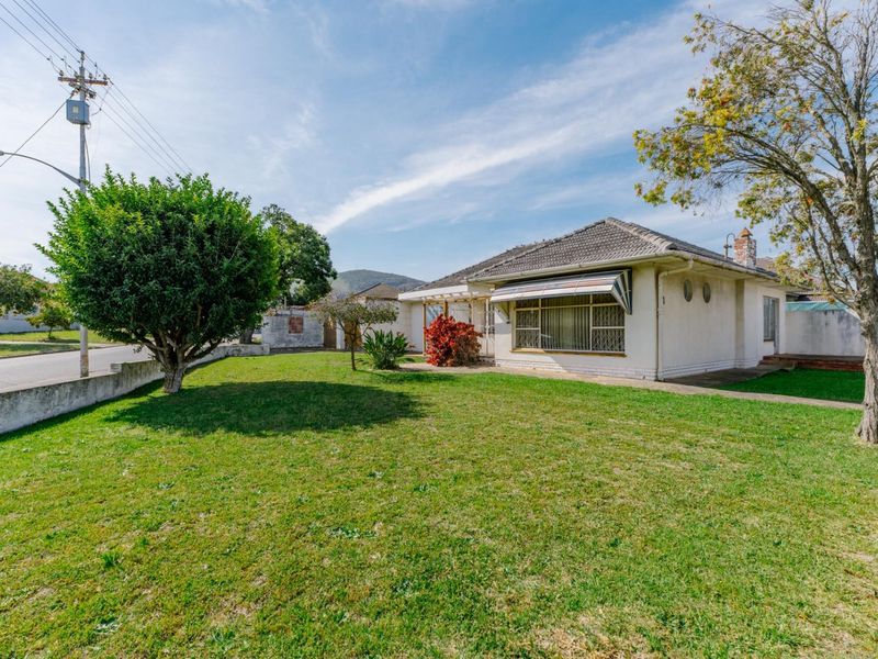 Front view of a single-story house featuring a tiled roof, security window bars, and a spacious front lawn with a concrete driveway.