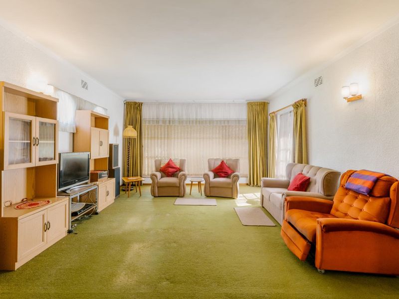 A spacious living room featuring large windows, wall-mounted lighting, and carpet flooring, offering a blank canvas for modern updates and interior design improvements.