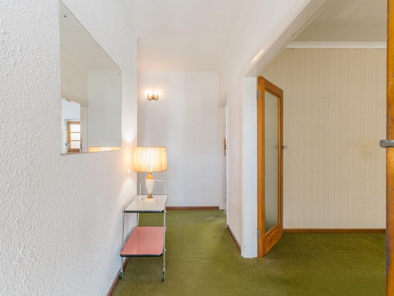 A dated hallway featuring textured walls, green carpeting, and a timber door, providing access to adjacent rooms.