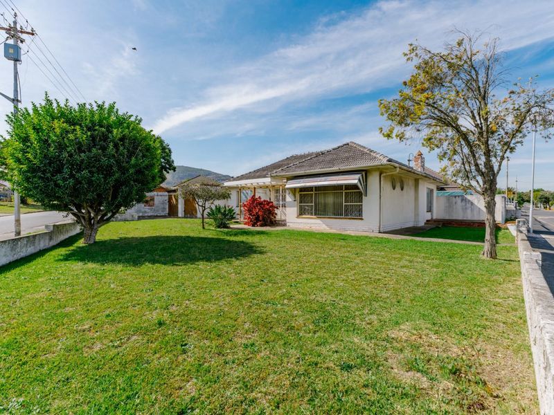 Front view of a single-story house featuring a tiled roof, window awnings, and a spacious front lawn with a concrete boundary wall.