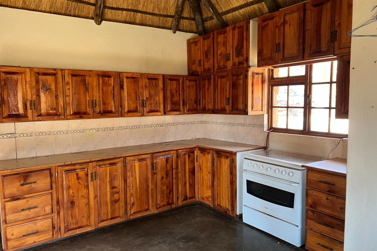 A rustic kitchen featuring extensive wooden cabinetry, a tiled backsplash, a freestanding stove, and a traditional thatched roof ceiling.