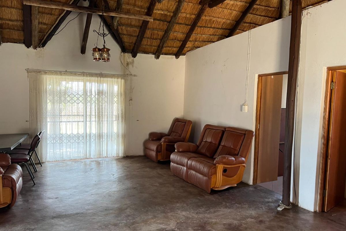 Spacious living area featuring a traditional thatched roof with exposed timber rafters, concrete flooring, and access to an outdoor area via sliding doors.