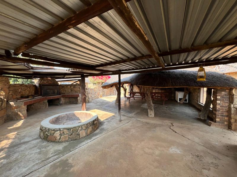 Spacious outdoor entertainment area featuring a built-in braai, stone fire pit, and a combination of thatched and corrugated metal roofing.