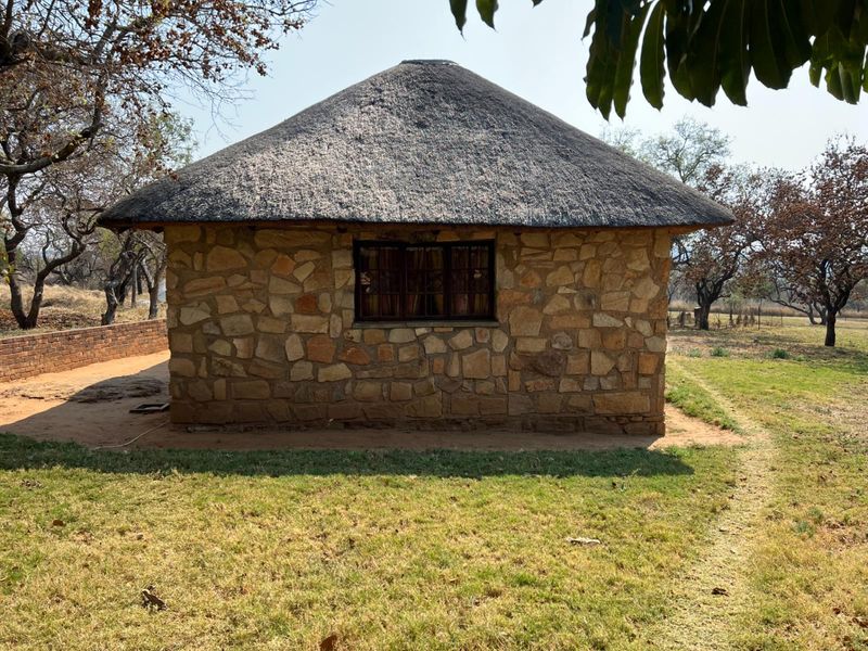 A charming rustic cottage featuring traditional stone masonry walls and a well-maintained thatched roof, set within a peaceful farm landscape.