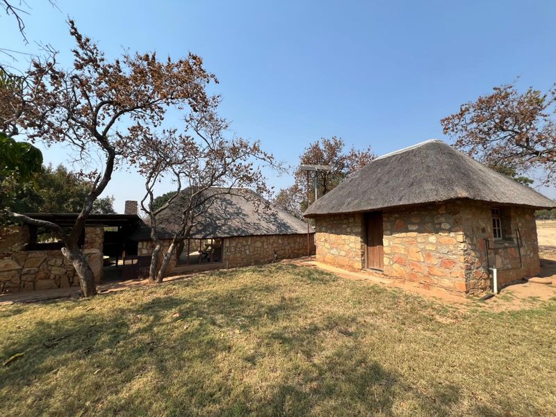 Exterior view of rustic stone farm buildings featuring traditional thatched roofs and a covered outdoor patio area set within a natural landscape.
