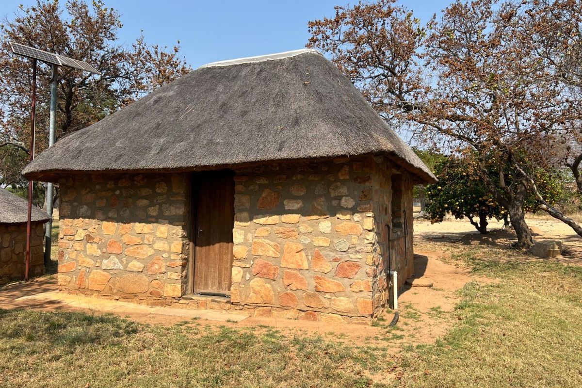 A rustic stone-built cottage with a traditional thatched roof, featuring an integrated solar panel setup in a rural farm setting.