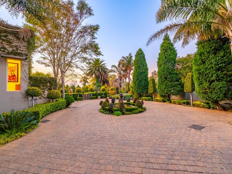 A beautifully landscaped front driveway featuring a central fountain, mature trees, and manicured hedges, providing an elegant and welcoming entrance to the property.
