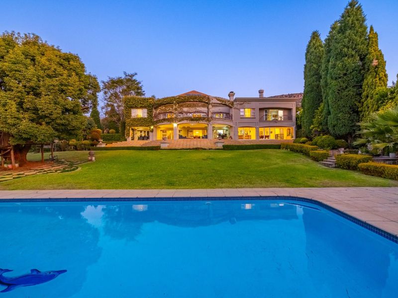 A stunning rear view of the property featuring a large swimming pool, expansive manicured lawn, and a spacious covered patio with balcony above.