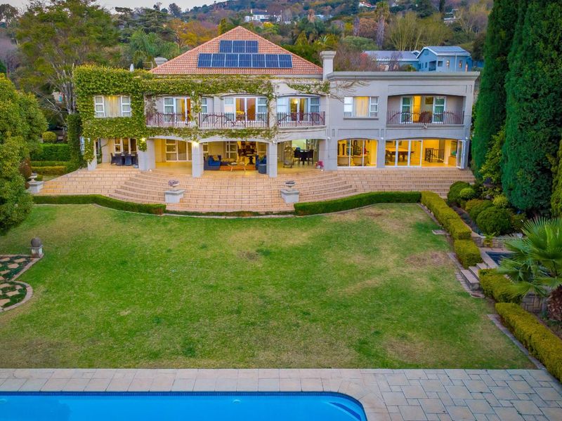 Spacious rear exterior view featuring a large landscaped garden, swimming pool, expansive paved patio, and a multi-level residence with solar panels and balconies.