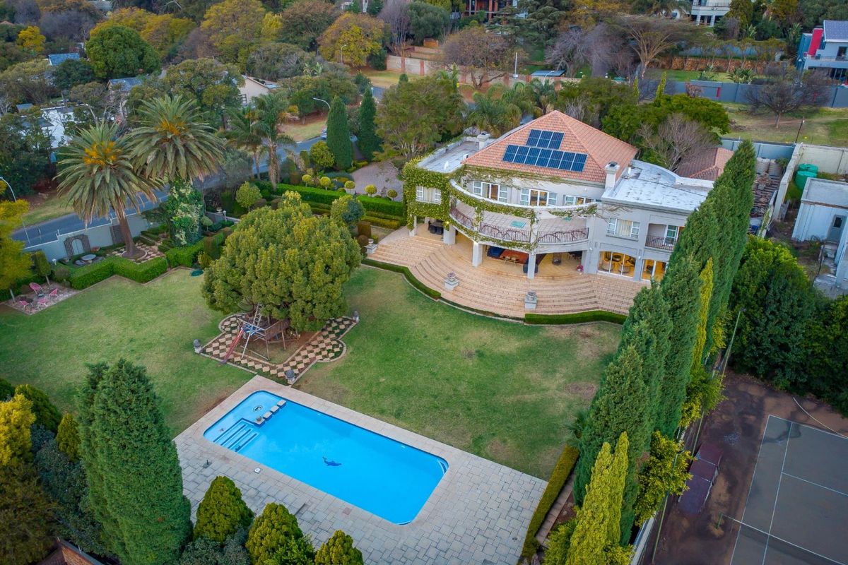 Aerial view of a large residential property featuring a swimming pool, tennis court, expansive landscaped garden, and a multi-level home with solar panels.