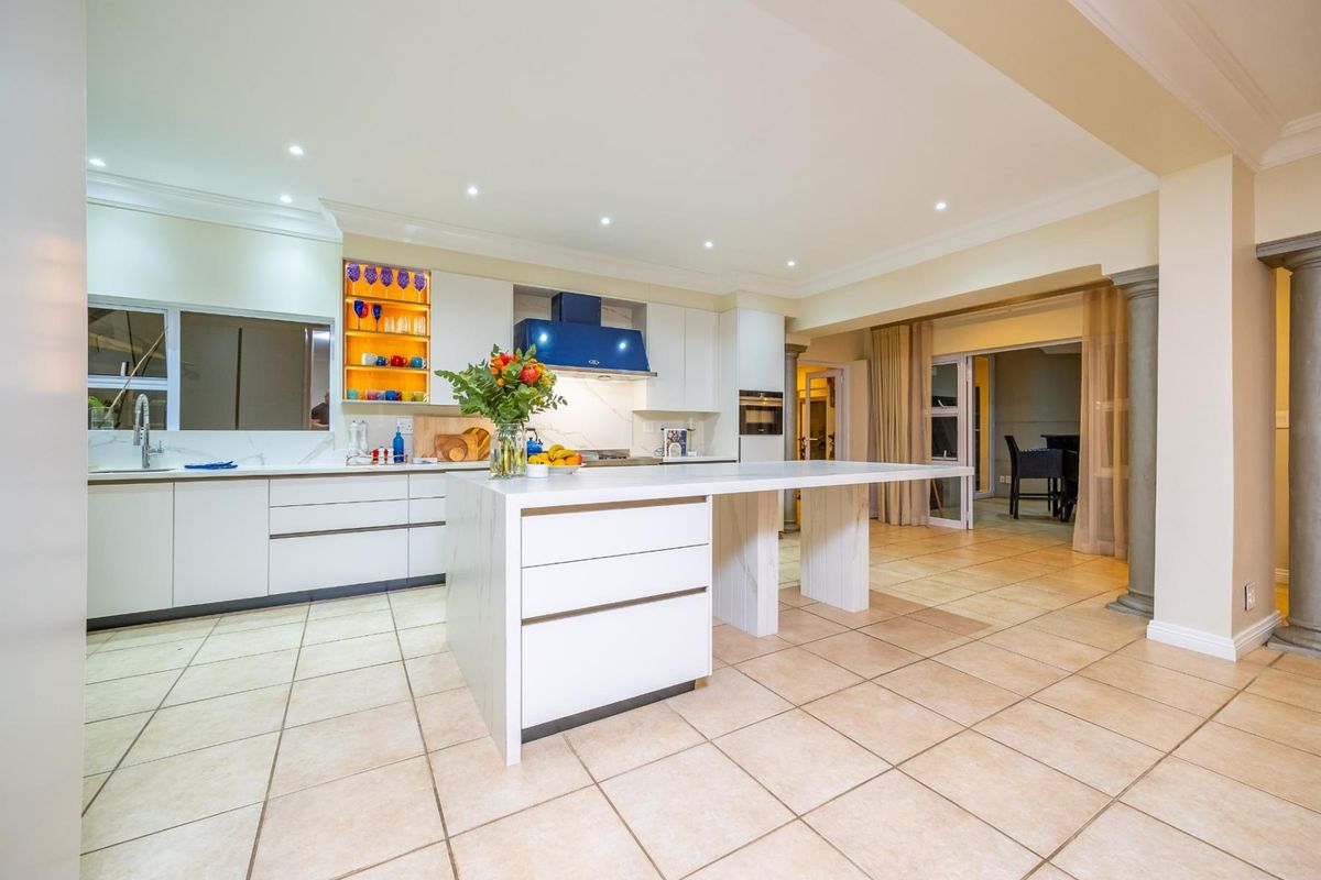 Modern kitchen featuring a central island, built-in oven, extractor fan, and stone countertops, finished with tiled flooring and recessed lighting.