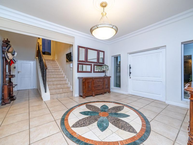 Spacious entrance foyer featuring decorative tiled flooring with a central inlay, a grand staircase with wrought iron balustrade, and elegant ceiling lighting.