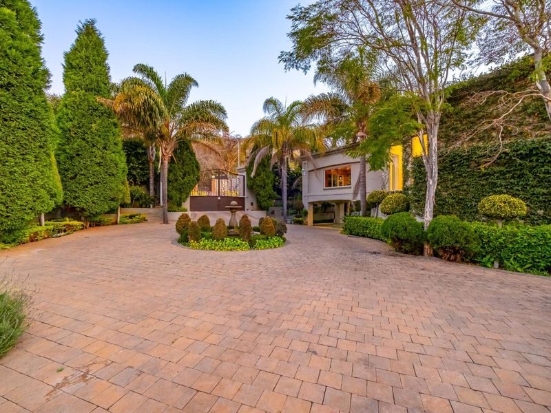 A spacious paved driveway leading to the front entrance, featuring a central stone fountain and mature landscaped gardens.