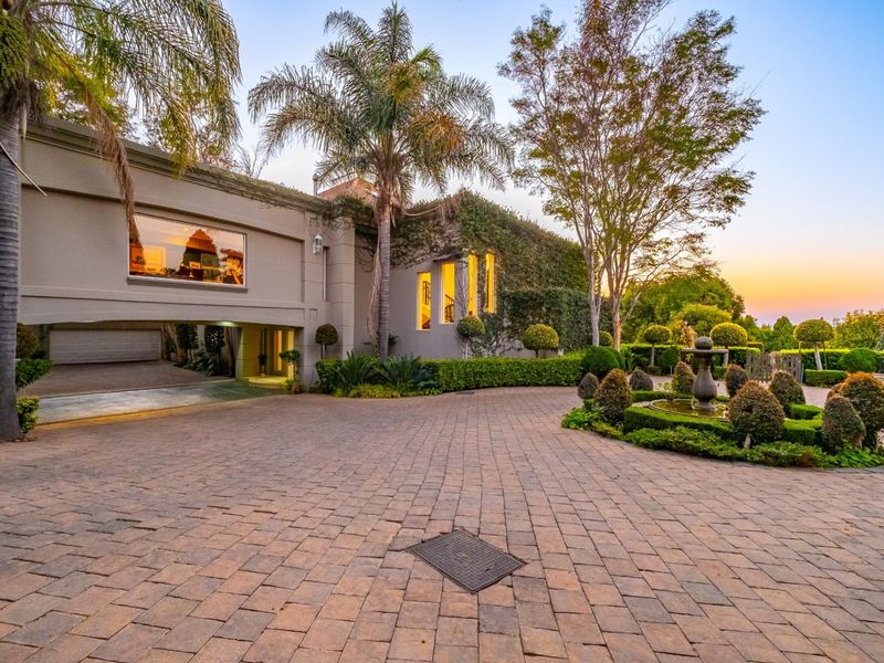 A well-maintained front exterior featuring a spacious paved driveway, landscaped garden with a central fountain, and a covered garage entrance.