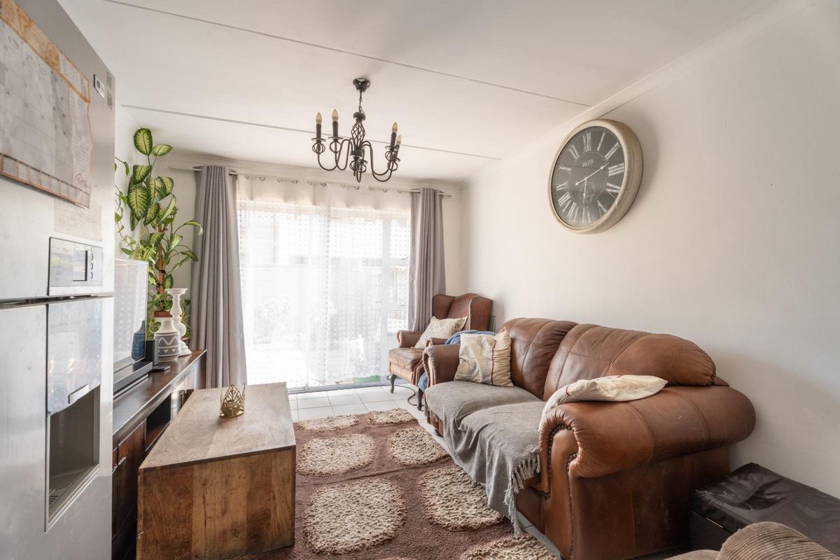 A cozy living room featuring tiled flooring, a central chandelier, and a sliding glass door providing natural light and access to the exterior.
