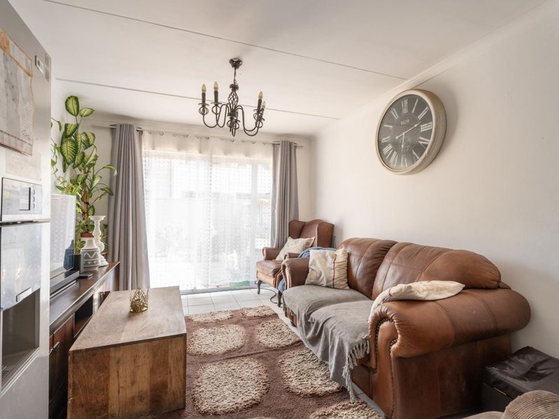 A cozy living room featuring tiled flooring, a central chandelier, and a sliding glass door providing natural light and access to the exterior.