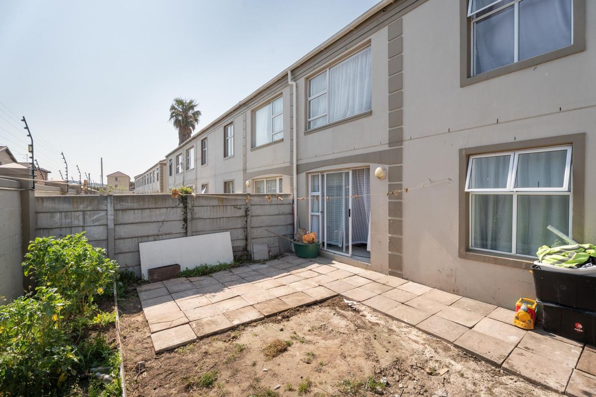 Rear exterior view of the apartment featuring a paved patio area, precast concrete boundary wall, and sliding door access to the living space.