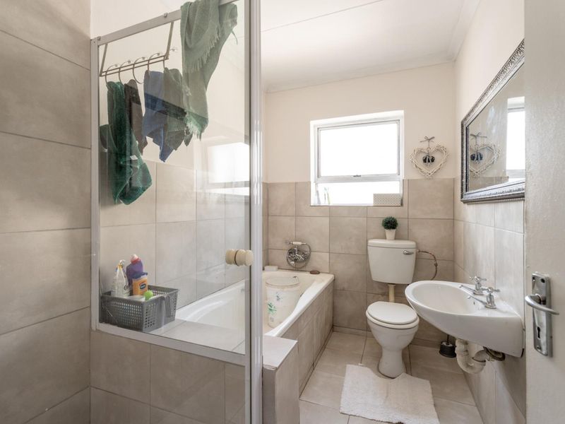 A functional bathroom featuring a bathtub with a shower screen, a pedestal basin, and a toilet, finished with neutral wall and floor tiles.