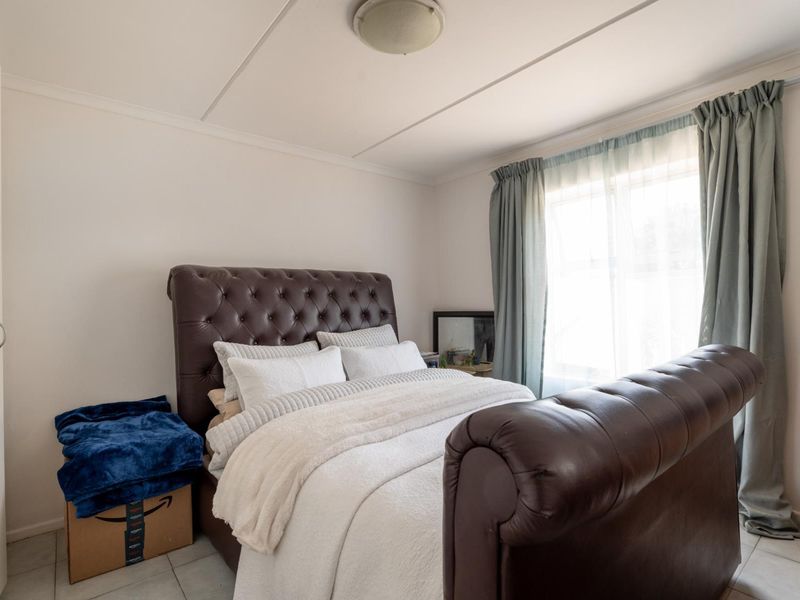 A bedroom featuring tiled flooring, a ceiling light fixture, and a built-in cupboard, with natural light entering through a window.