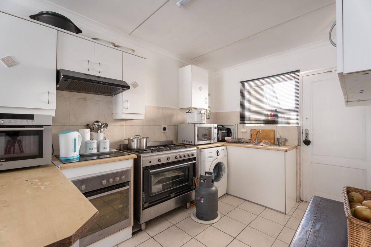 Functional kitchen featuring white cabinetry, gas stove with extractor, tiled backsplash, and integrated laundry plumbing, offering a practical layout for daily meal preparation.