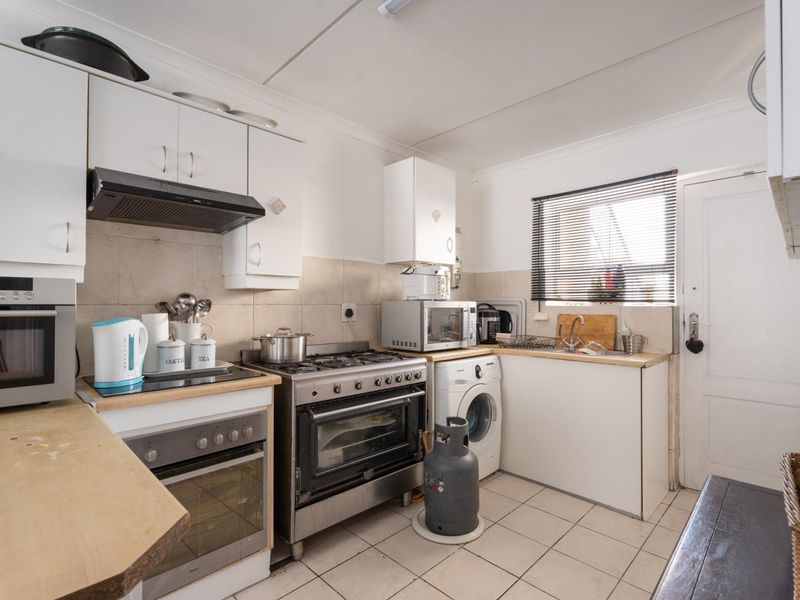 Functional kitchen featuring white cabinetry, gas stove with extractor, tiled backsplash, and integrated laundry plumbing, offering a practical layout for daily meal preparation.