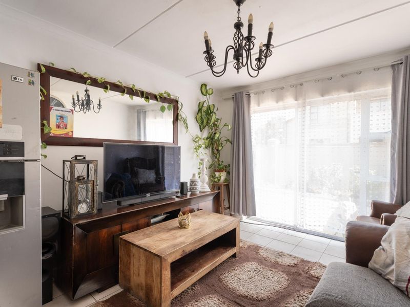 A living room featuring tiled flooring, a wrought iron chandelier, and a large sliding glass door providing access to the exterior.