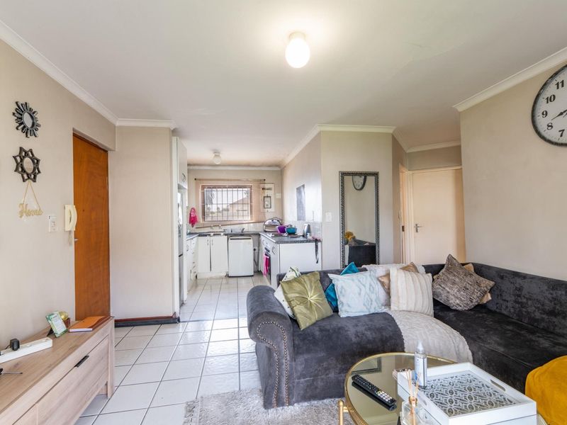 Open plan living area featuring tiled flooring and a functional kitchen space with built-in cabinetry and a window with security bars.