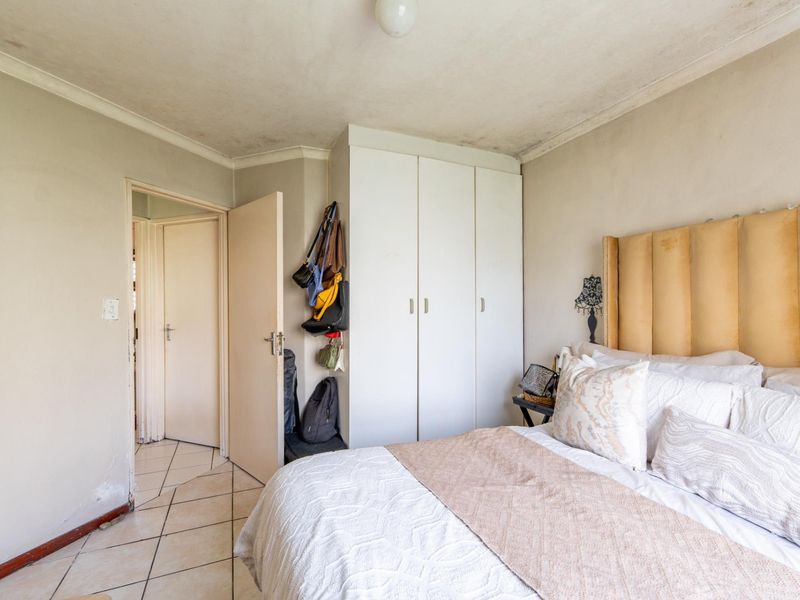 A bedroom featuring built-in wardrobes and tiled flooring, showing signs of wear including ceiling staining and wall damage requiring maintenance.