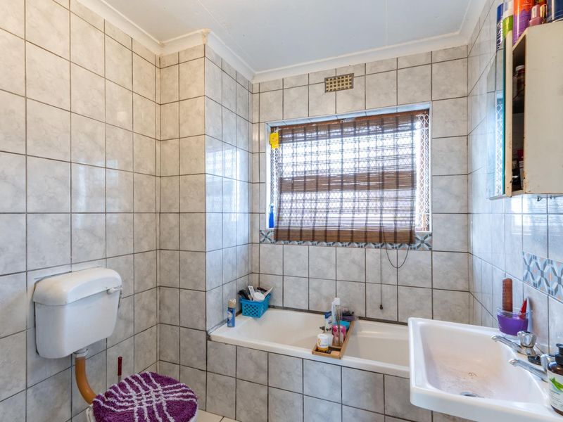 A compact bathroom featuring a bathtub, wall-mounted toilet cistern, and pedestal washbasin, finished with dated ceramic wall tiling.