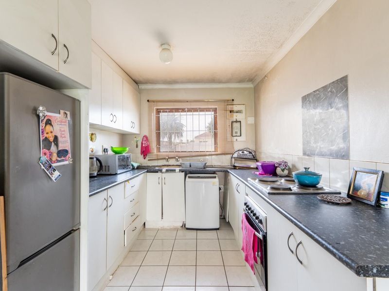 A functional galley-style kitchen featuring white cabinetry, dark laminate countertops, built-in oven and hob, and tiled flooring, offering potential for modernization.
