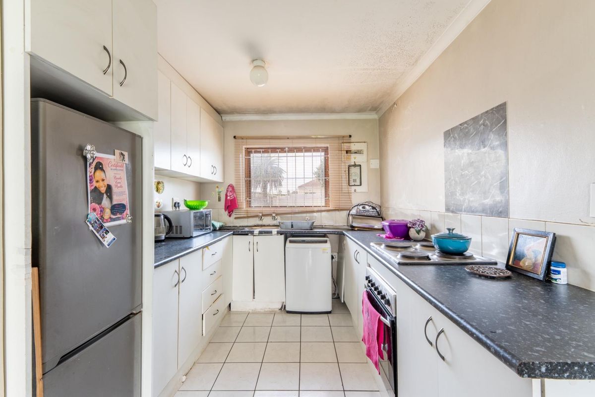 A functional galley-style kitchen featuring white cabinetry, dark laminate countertops, built-in oven and hob, and tiled flooring, offering potential for modernization.